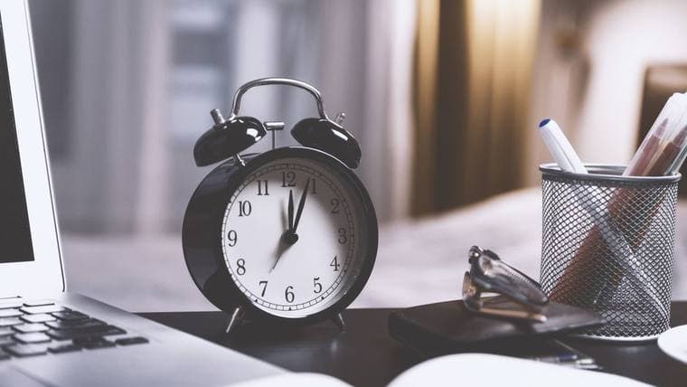 An alarm clock beside a laptop on a desk